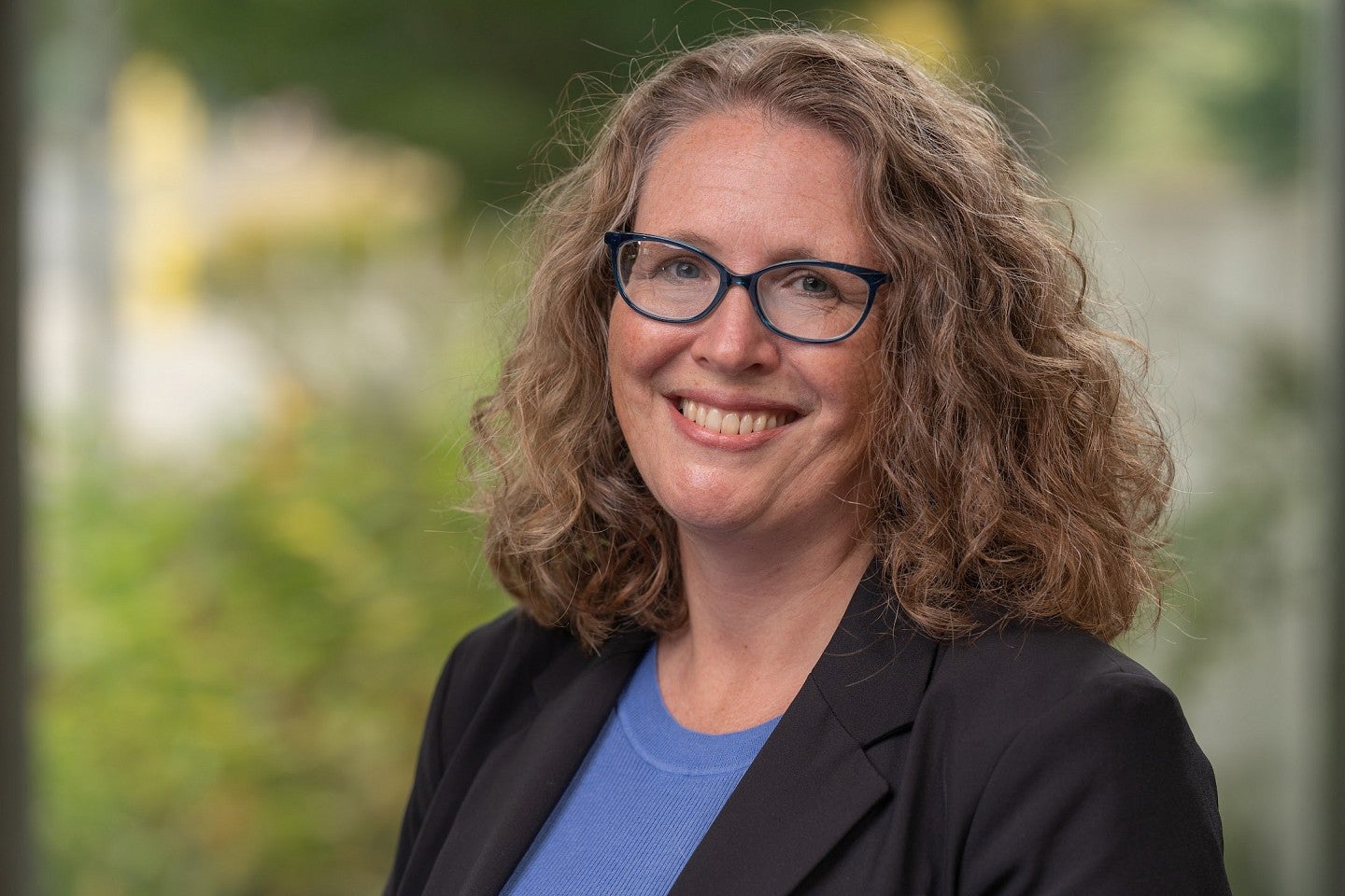 Headshot of Elly Vandegrift standing in front of greenery