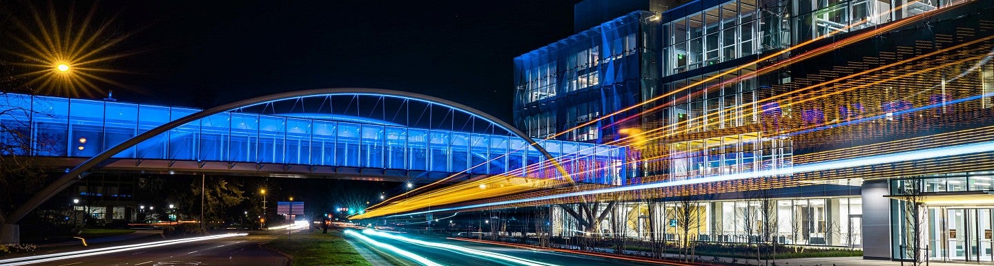 Long exposure photo of a lit up sky bridge at night connecting to a building