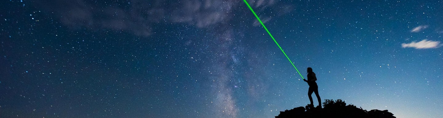 Person on rock at night, starry sky above, green light beaming from them