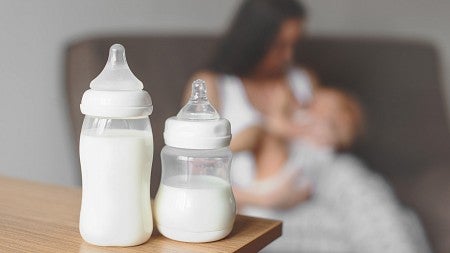 Manual breast pump and bottle with breast milk on the background of mother holding in her hands and breastfeeding baby