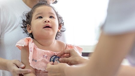 An infant wearing a pink shirt being examined by a doctor with a stethoscope 