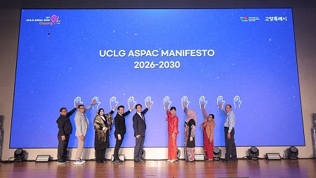 Nine Mayor's Academy participants standing giving a high five to a hand on a blue screen