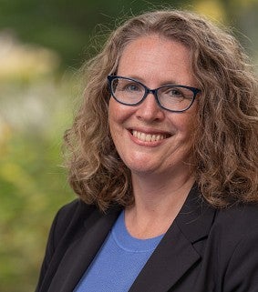 Headshot of Elly Vandegrift standing in front of greenery